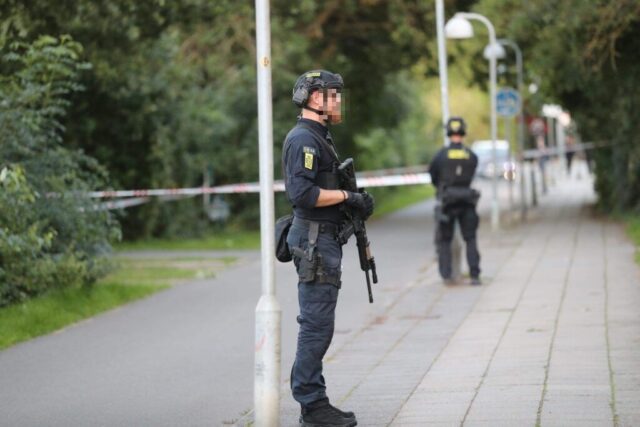 Mand med skimaske vender sig om og skyder to personer på gaden