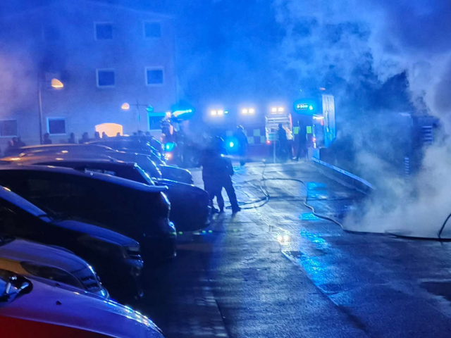 Røg og flammer på parkeringsplads i nat